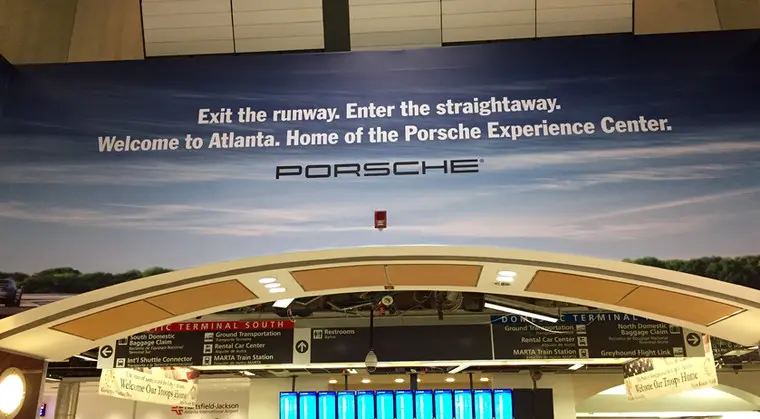 Porsche advertisement at Atlanta airport reading “Exit the runway. Enter the straightaway. Welcome to Atlanta. Home of the Porsche Experience Center.